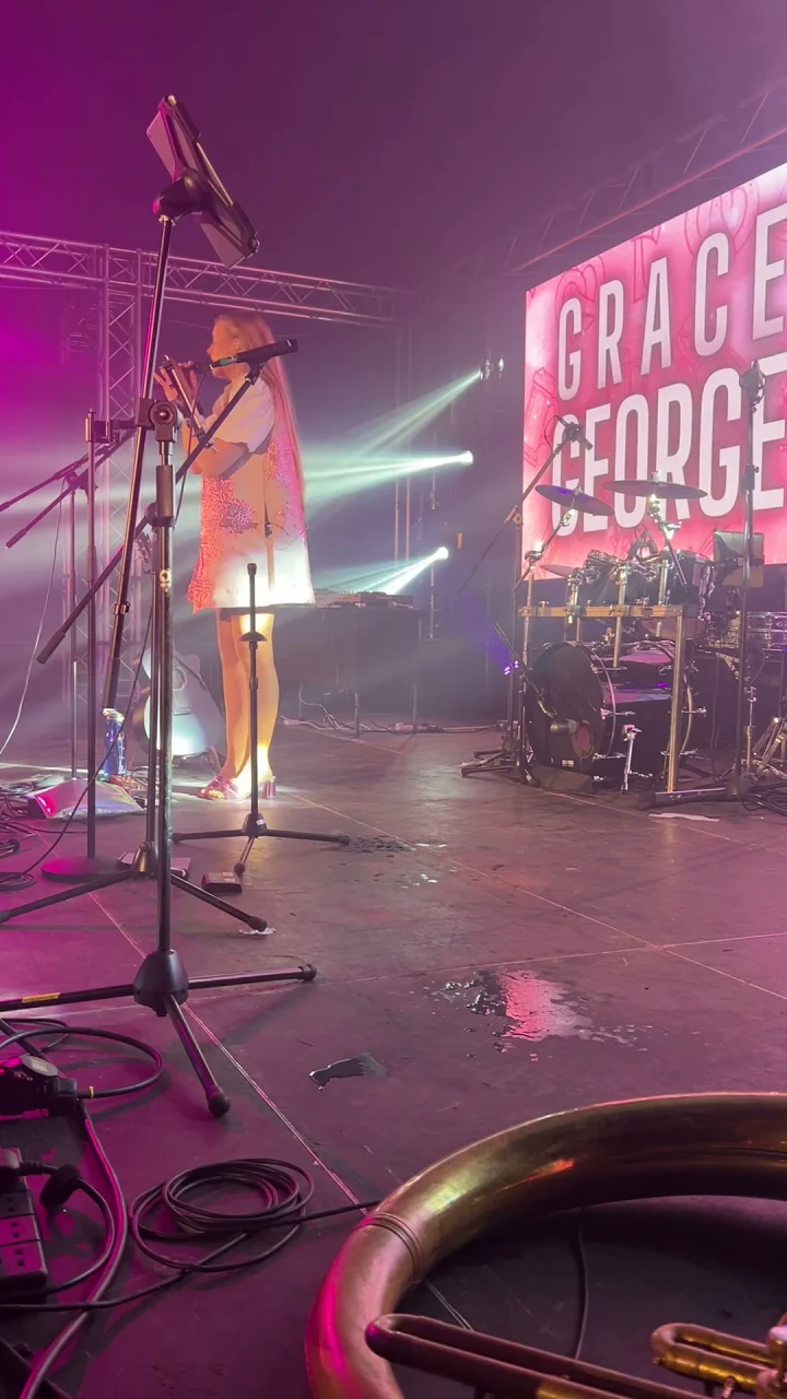 Grace George singing at a microphone on a large pink-lit stage, her name in big letters on the screen.