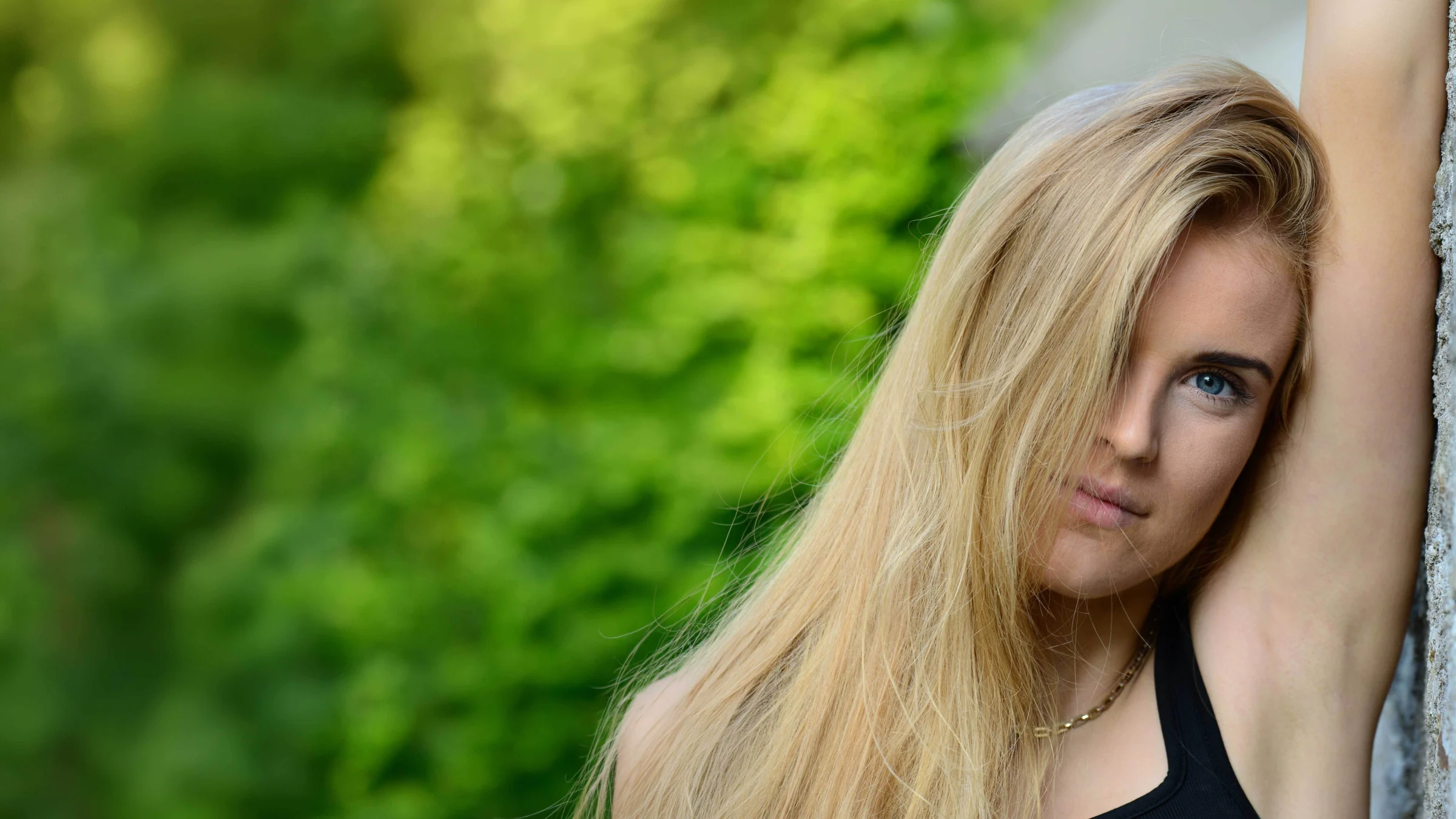 Grace George leaning on a grey stone wall with one arm raised, long blonde hair falling over one eye.